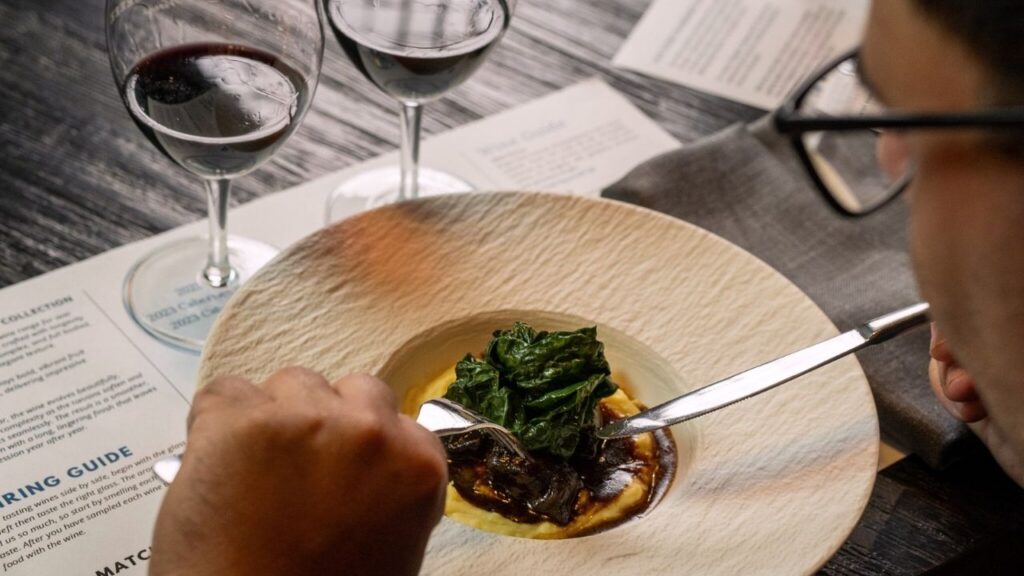 Slow-cooked lamb with mash and greens beside paired red wines